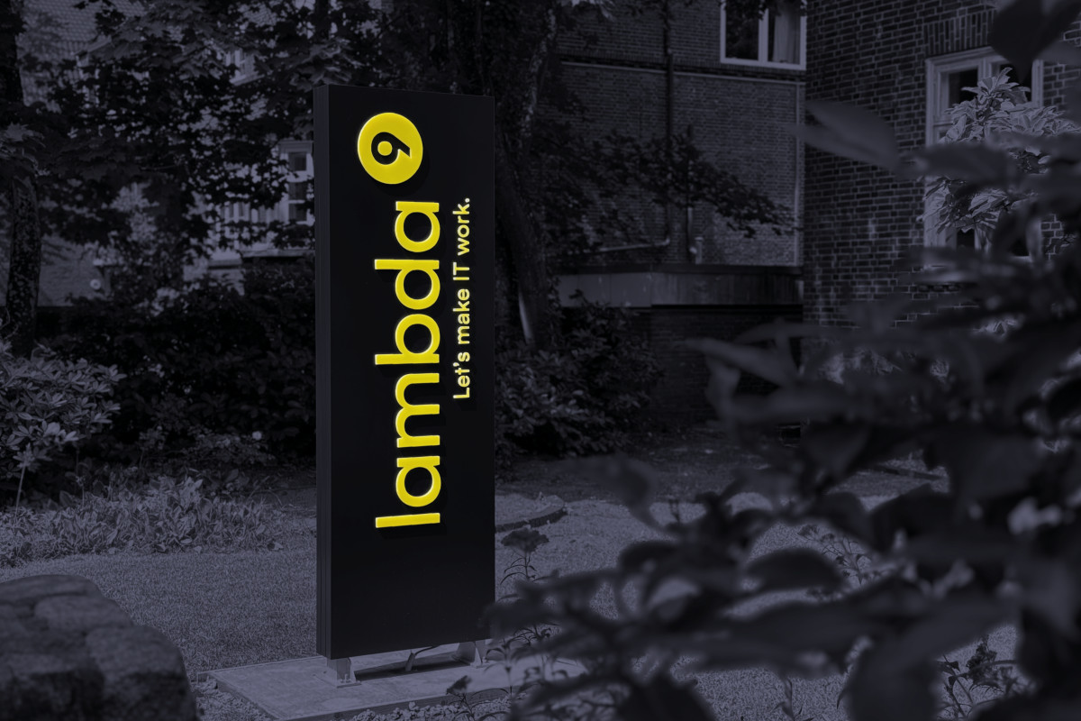 Ein Leuchtschild mit dem Logo der lambda9 steht in einem Vorgarten.